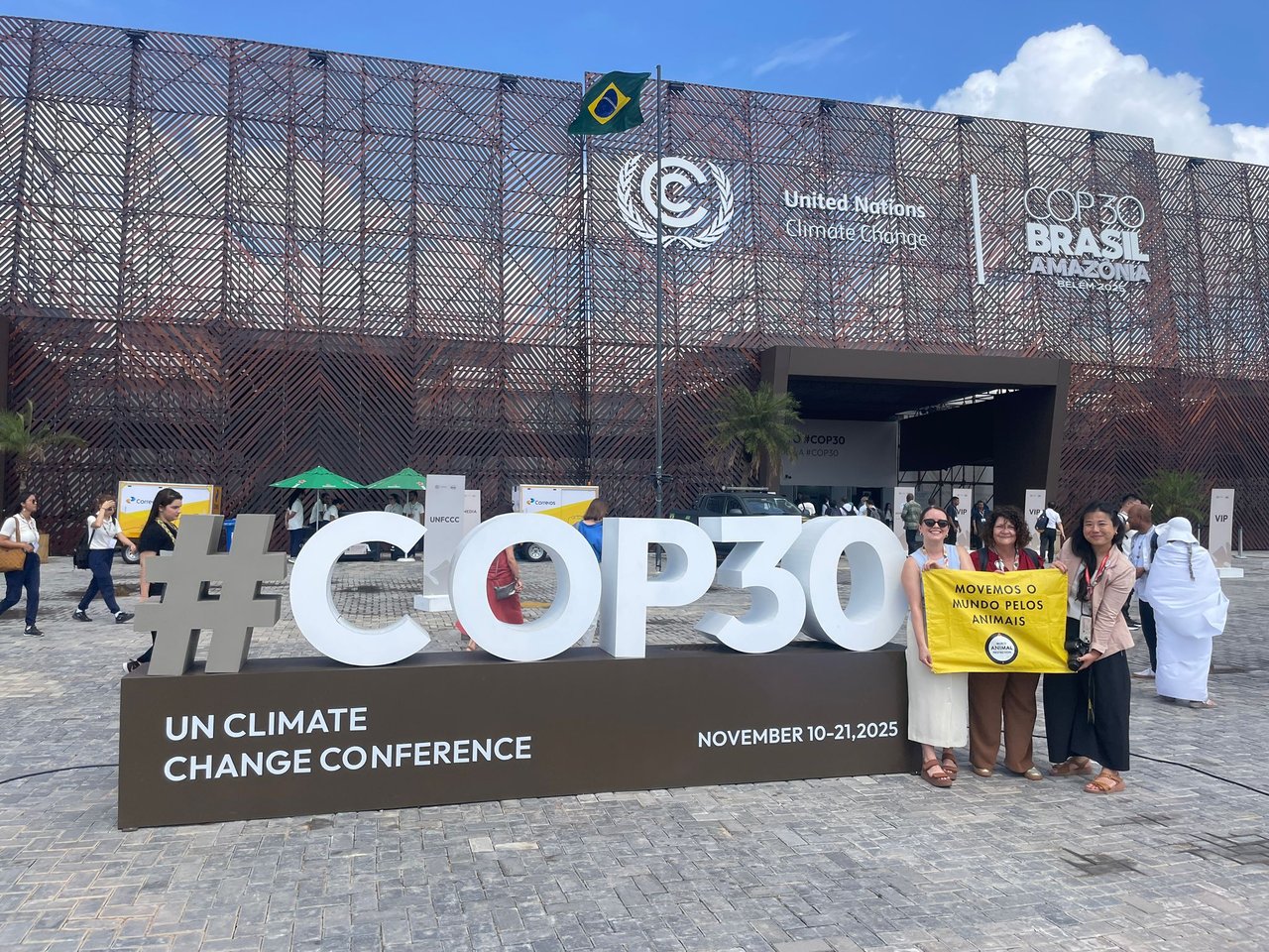 Miembros de World Animal Protection junto al gran letrero de #COP30 frente al recinto de la conferencia climática en Belém, sosteniendo una pancarta amarilla.
