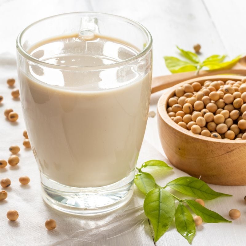 Un vaso de leche de soja junto a los granos de la soja.