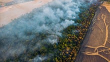 Vista aérea de la deforestación en la Amazonía, con humo elevándose del bosque incendiado junto a tierras agrícolas recién despejadas.